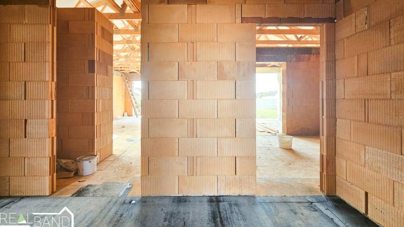 Der Innenraum eines im Bau befindlichen Einfamilienhauses mit unverputzten Ziegelwänden und Blick nach draußen.