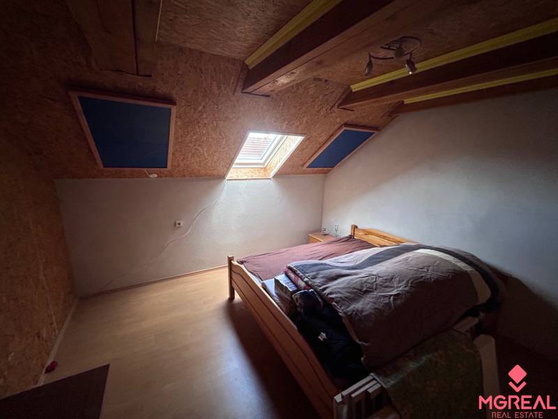 Dachbodenschlafzimmer mit Bett und Dachfenster in einem Einfamilienhaus, Boden mit Holzdekor.