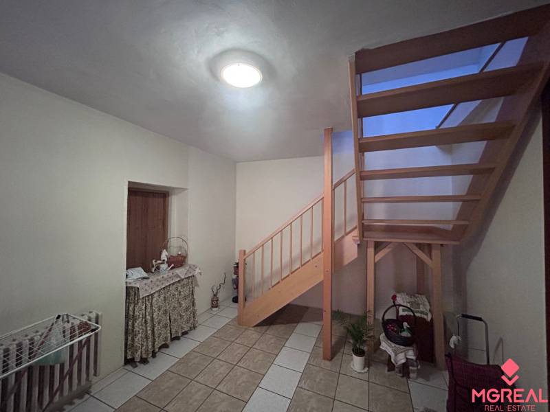 Innenraum eines Einfamilienhauses mit Holztreppe, Tisch und Boden aus Keramikfliesen.