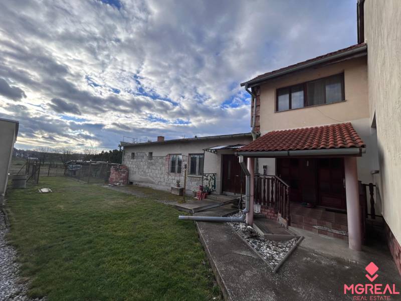 Ein Einfamilienhaus in Zbehy mit Rasen, Garten und einem Steinweg unter einem bewölkten Himmel.