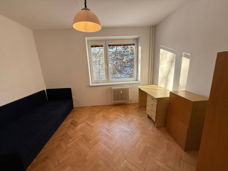 Ein Zimmer in einer 3-Zimmer-Wohnung mit einem Holzboden, einem blauen Sofa und einem Schreibtisch.