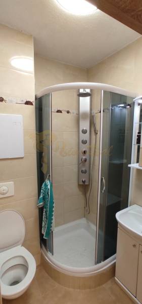 Badezimmer in einer Einzimmerwohnung mit Eckdusche, Waschbecken und WC.