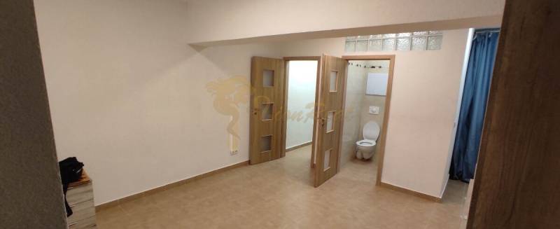 Innenraum einer Einzimmerwohnung mit Keramikfliesen und sichtbarem Badezimmer durch die Tür.