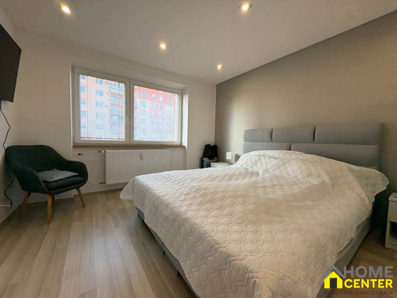 Schlafzimmer in einer 2-Zimmer-Wohnung mit Holzboden, einem bequemen Sessel und einem großen Fenster.