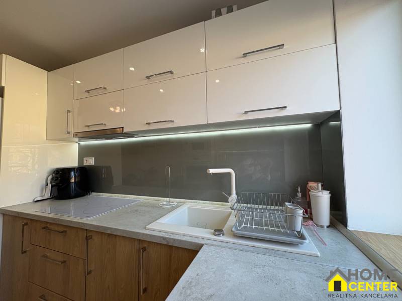 Küche in einer 2-Zimmer-Wohnung mit hellen Schränken und Beleuchtung über der Arbeitsplatte.