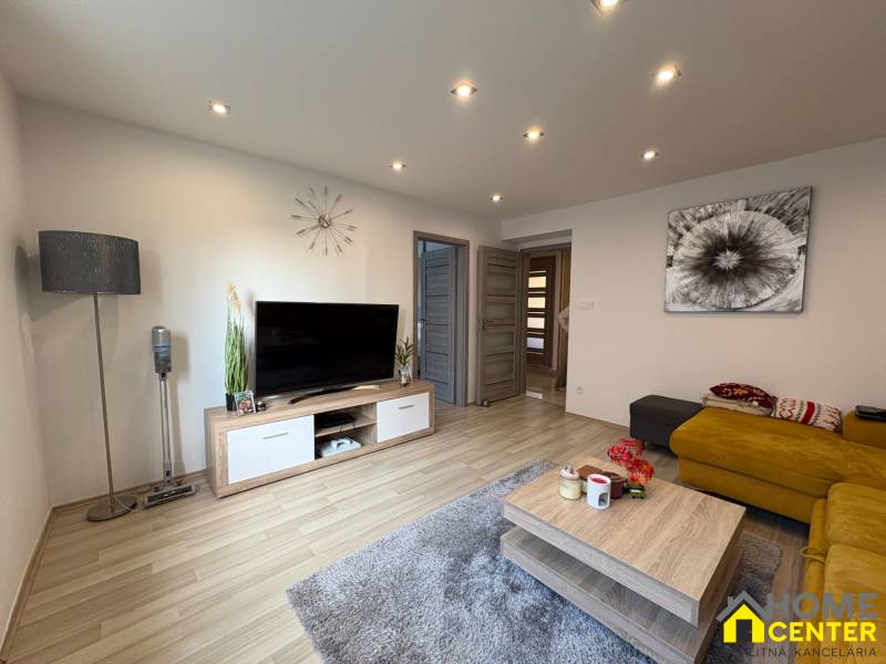 Wohnzimmer in einer 2-Zimmer-Wohnung mit Holzboden, Fernseher und gelbem Sofa.