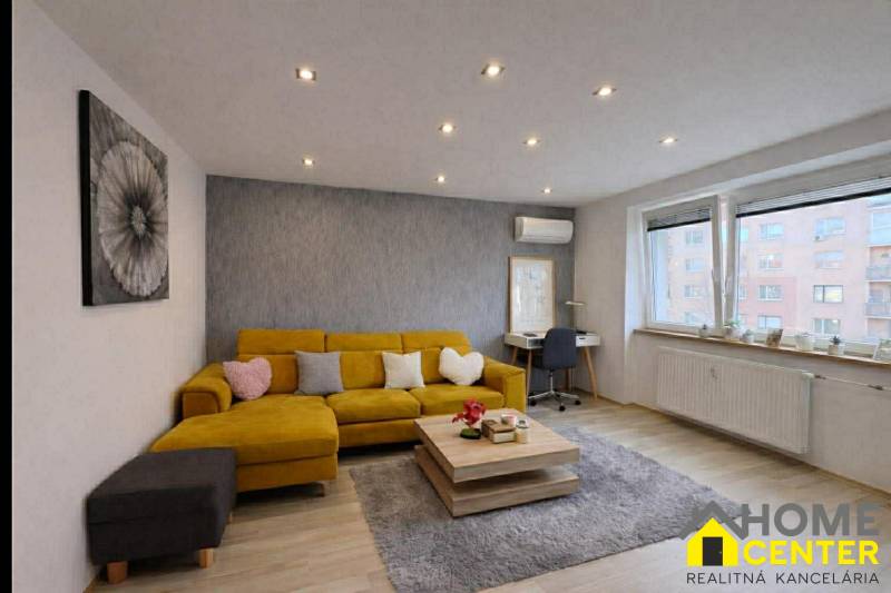 Wohnzimmer in einer Zweizimmerwohnung mit Sofa, Holzboden, grauer Teppich.