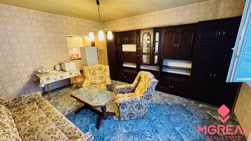 Wohnzimmer in einer Zweizimmerwohnung mit älteren Möbeln und einem Teppich auf dem Boden.