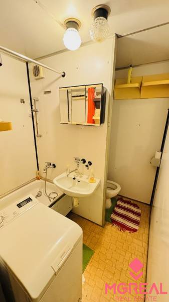Badezimmer mit Waschbecken, Waschmaschine und Toilette in einer 2-Zimmer-Wohnung, einfache Aufbewahrungslösungen.