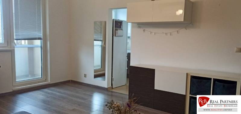 Wohnzimmer in einer Zweizimmerwohnung mit Holzboden, weißen Möbeln und einem Spiegel.