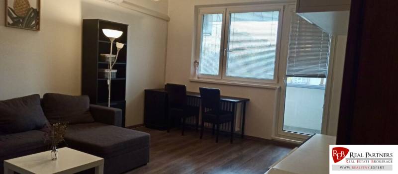 Wohnzimmer in einer Zweizimmerwohnung mit Ecksofa und Holzboden.