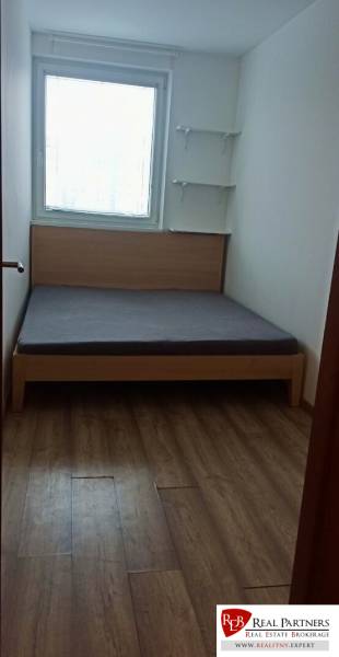 Schlafzimmer in einer 2-Zimmer-Wohnung mit Bett, Regalen und Boden in Holzoptik.