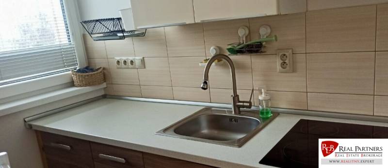 Küche in einer 2-Zimmer-Wohnung mit Spüle, Glaskeramikkochfeld und Korb am Fenster.