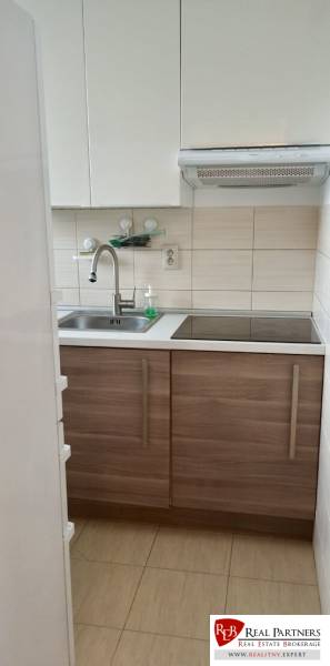 Küche mit weißen Schränken und Edelstahlspüle in einer 2-Zimmer-Wohnung.