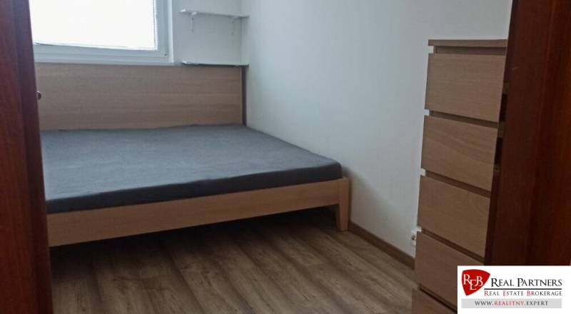 Schlafzimmer in einer 2-Zimmer-Wohnung mit Bett, Holzboden, Kommode und Regalen.