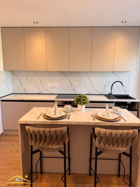 Küche mit Bartresen, Holzboden und hellem Mobiliar in einer Zweizimmerwohnung.