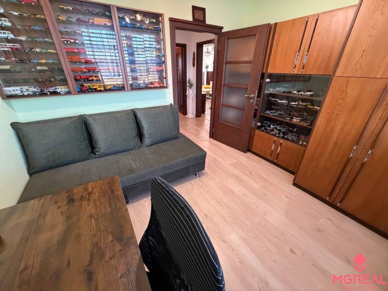 Ein Zimmer mit einem Sofa, einer Vitrine mit Modellen und einem Boden mit Holzdekor in einer 3-Zimmer-Wohnung.