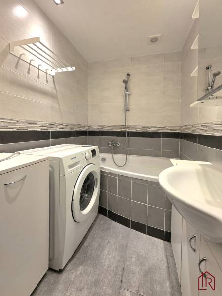 Badezimmer mit Badewanne, Waschmaschine und Fliesen in einer 2-Zimmer-Wohnung.