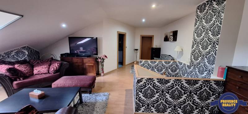 Wohnzimmer in einem Einfamilienhaus mit Sofa, gemusterten Tapeten und Fernseher.