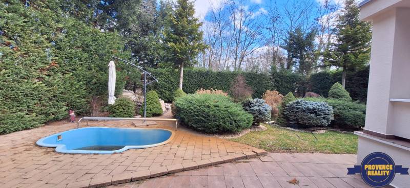 Ein Einfamilienhaus in Komárno mit einem kleinen Pool und einem gepflegten Garten, umgeben von Bäumen.