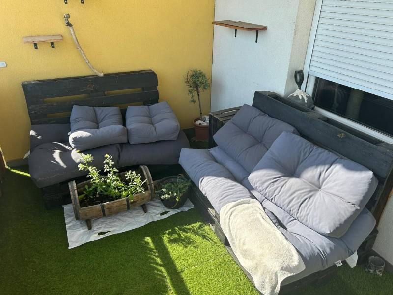In der 3-Zimmer-Wohnung gibt es eine Terrasse mit Palettenmöbeln, Kissen und Pflanzen auf Kunstrasen.