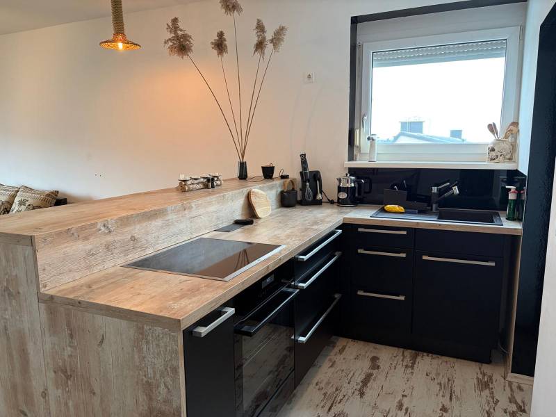 Küche in einer 3-Zimmer-Wohnung mit schwarzen Schränken und einem Boden in Holzoptik.