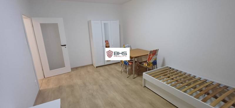 Ein Zimmer in einer 3-Zimmer-Wohnung mit einem weißen Schrank, einem Bett und einem Tisch auf einem Boden mit Holzdekor.