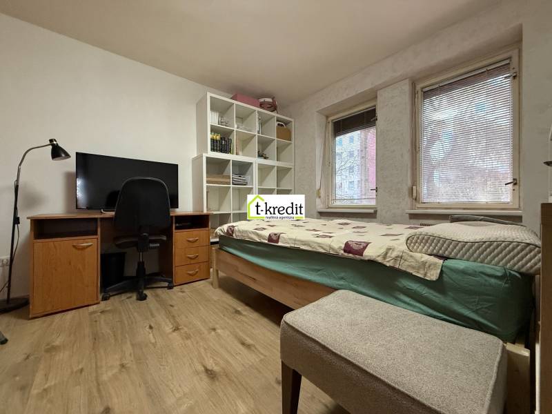 Ein Zimmer in einer 2-Zimmer-Wohnung mit einem Bett, einem Schreibtisch und einem Boden mit Holzdekor.