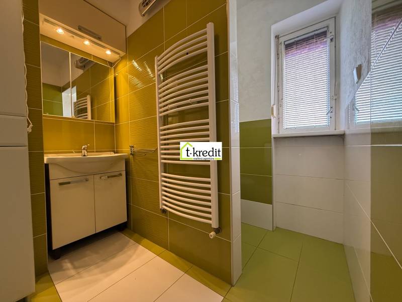 Badezimmer in einer 2-Zimmer-Wohnung mit Waschbecken, Spiegel und grün-weißen Fliesen.