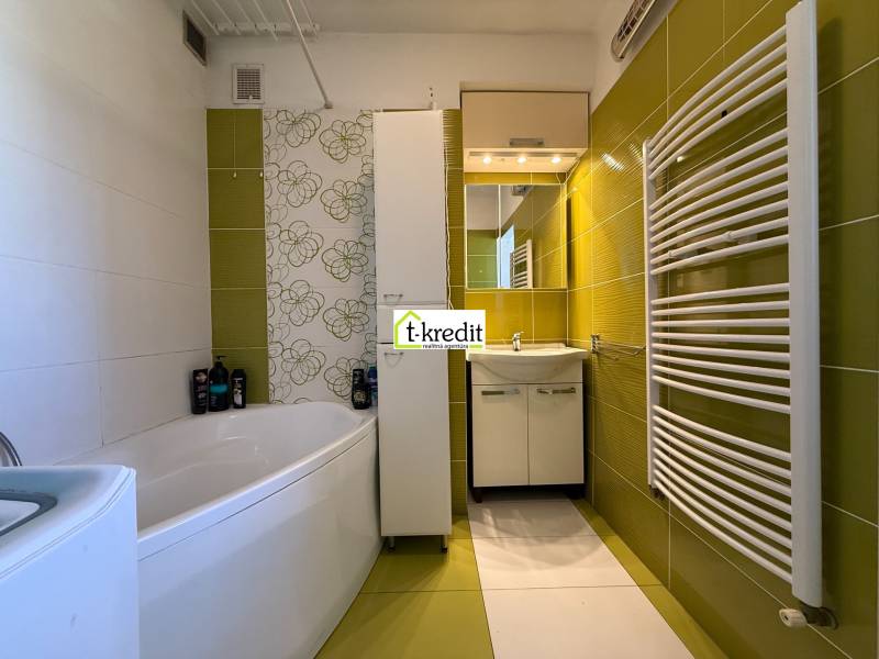 Ein Badezimmer in einer 2-Zimmer-Wohnung mit grünen Fliesen, einer Badewanne und einem modernen Heizkörper.