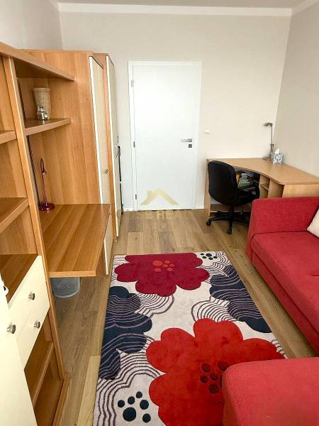 Ein Zimmer in einer 3-Zimmer-Wohnung mit einem Boden in Holzoptik, einem roten Teppich und einem Schreibtisch.