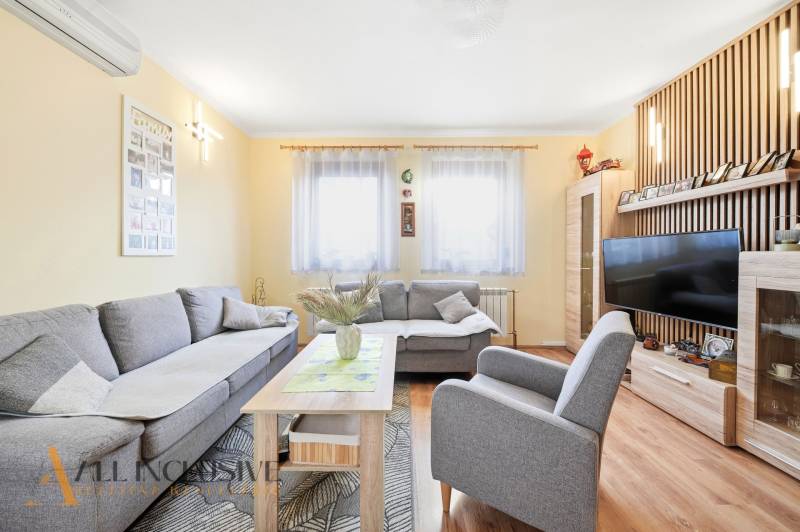 Wohnzimmer in einem Einfamilienhaus mit einem bequemen grauen Sofa und einem Boden in Holzoptik.