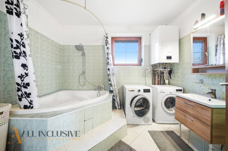 Badezimmer mit Badewanne, Dusche, Waschmaschine und Trockner in einem Einfamilienhaus.