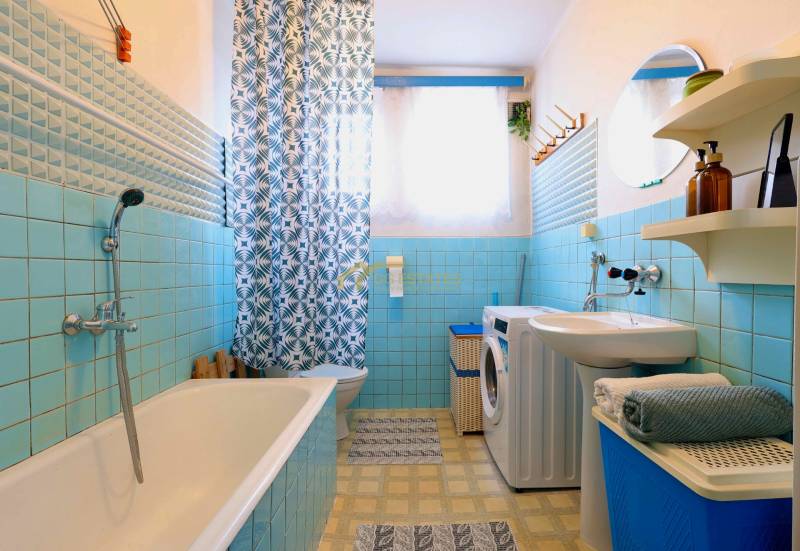 Ein Badezimmer in einem Einfamilienhaus mit blauen Fliesen, einer Badewanne, einer Waschmaschine und einem gemusterten Vorhang.