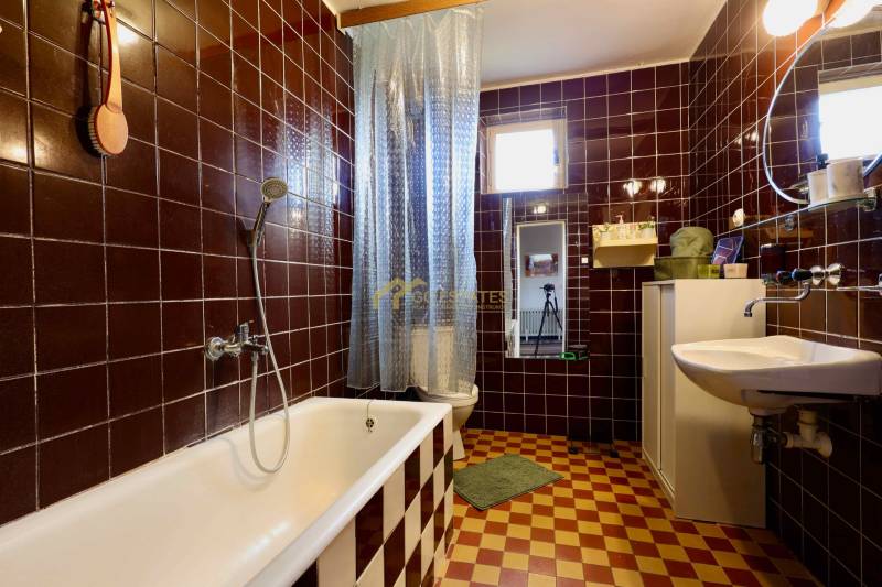 Ein Badezimmer in einem Einfamilienhaus mit stilvollen dunkelbraunen Fliesen und einer klassischen Badewanne.