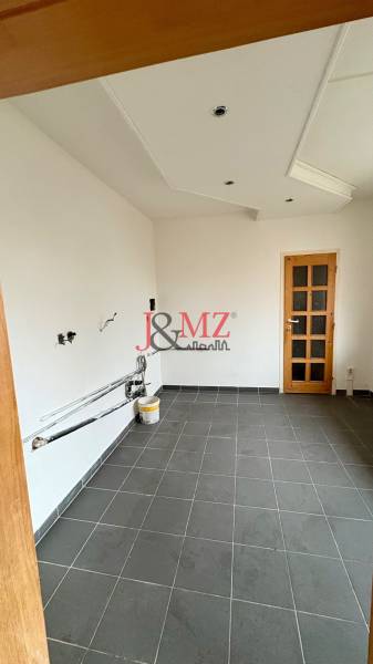 Ein leerer Raum in einer 2-Zimmer-Wohnung, dunkler Fliesenboden, weiße Wände, Holztüren.