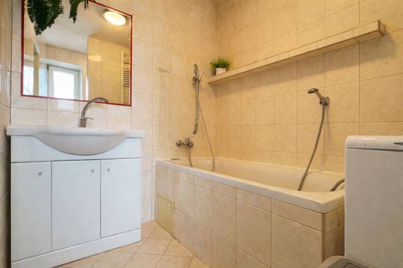 Badezimmer in einer 2-Zimmer-Wohnung mit Badewanne, Waschbecken, Spiegel und beigen Fliesen.
