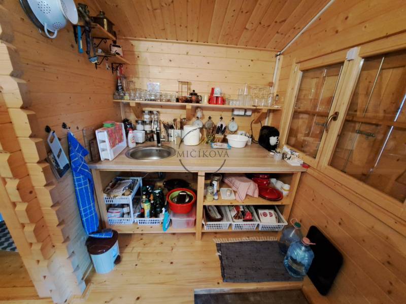 Holzküche mit Geräten, Regalen und Spüle im Garteninterieur.