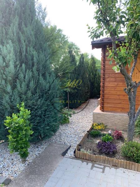 Gärten in Dolné Krškany, Nitra mit gepflegten Nadelbäumen und einem hölzernen Gartenhäuschen.