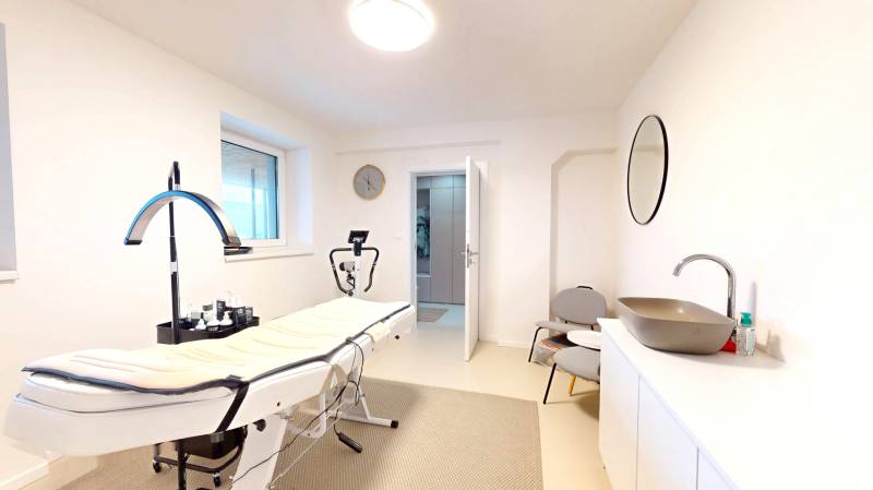 Innenraum eines Einfamilienhauses mit Massagetisch, Waschbecken, Spiegel und Stühlen.