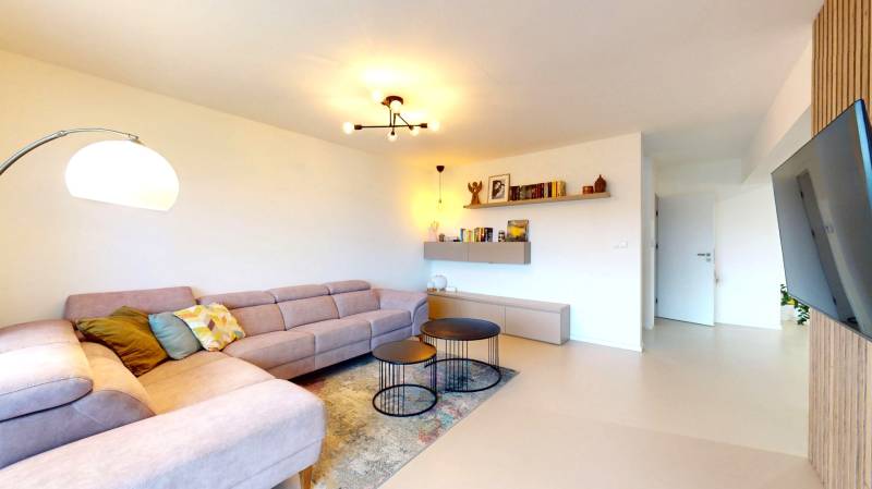 Wohnzimmer in einem Einfamilienhaus mit einer Eckcouch, runden Tischen und einem Boden in Holzoptik.