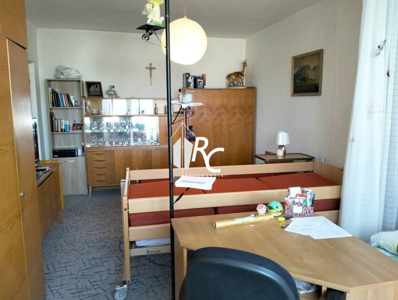 Ein Zimmer in einer 2-Zimmer-Wohnung mit Möbeln, einem Bett und Dekorationen auf den Regalen.