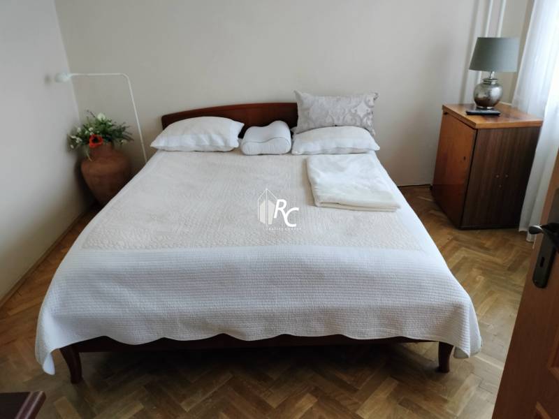 Schlafzimmer mit Doppelbett, Holzboden und Nachttisch in einer Zweizimmerwohnung.