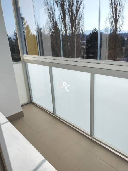 Ein verglaster Balkon in einer 2-Zimmer-Wohnung mit Blick auf Bäume und Berge.