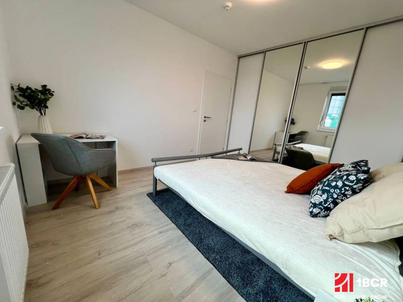 Schlafzimmer in einer 2-Zimmer-Wohnung mit Bett, Schreibtisch und Spiegelschrank.