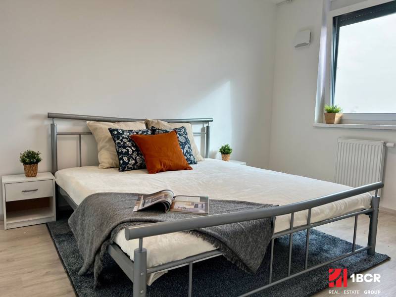 Schlafzimmer in einer 2-Zimmer-Wohnung mit einem Metallbett, Holzboden, einfachen Dekorationen.
