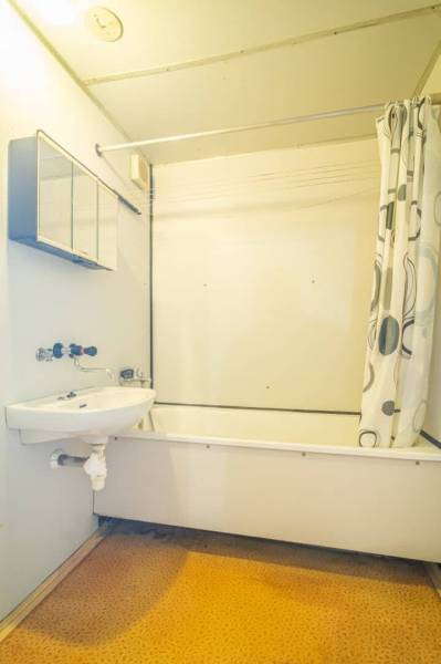 Badezimmer mit Badewanne und Duschvorhang in einer 2-Zimmer-Wohnung, helle Wände, orangener Boden.