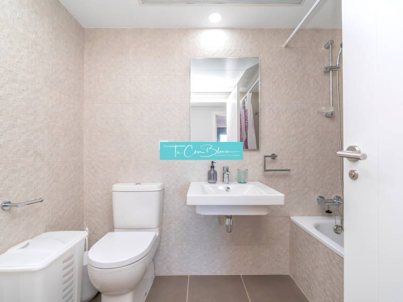 Badezimmer in einer 2-Zimmer-Wohnung mit Toilette, Waschbecken, Badewanne und beigen Fliesen.