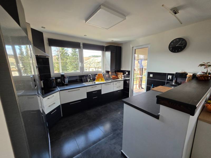 Eine Küche in einem Einfamilienhaus mit Keramikboden, dunklen Möbeln und großen Fenstern.