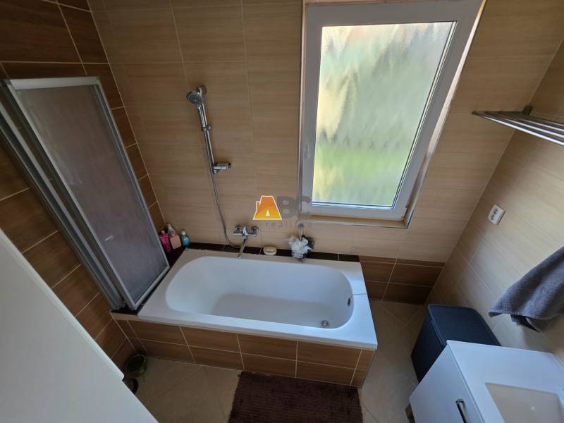 Ein Badezimmer in einem Einfamilienhaus mit einer Badewanne und einem Fenster, gefliest mit braunen Fliesen.